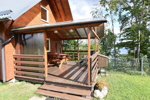 A wooden cabin with a covered deck, a picnic table, and a fenced yard. - Cottage in a Quiet Location by the Lake Mausz, Parchowo in Kashubia (Parchowo)