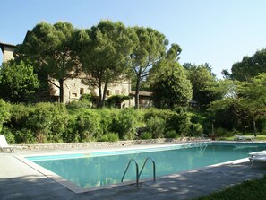 A swimming pool with a stone deck, surrounded by lush greenery and trees. - Cosy Apartment in Mantignana With Private Terrace (Corciano)