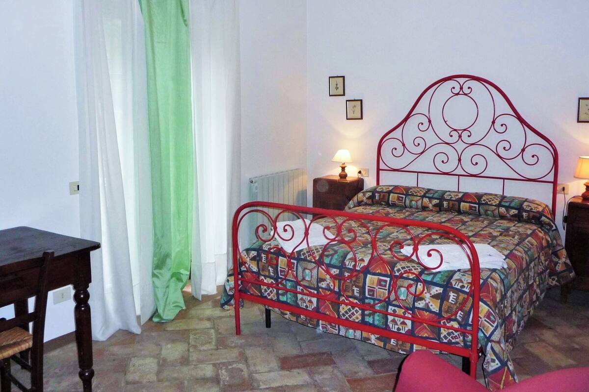 Une chambre avec un lit en métal, un bureau en bois et une chaise. Il y a deux tables de chevet avec des lampes.