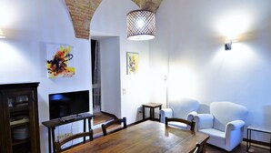 A dining area with a wooden table, white chairs, a TV, and artwork on the walls. - Cosy Apartment in Mantignana With Private Terrace (Corciano)