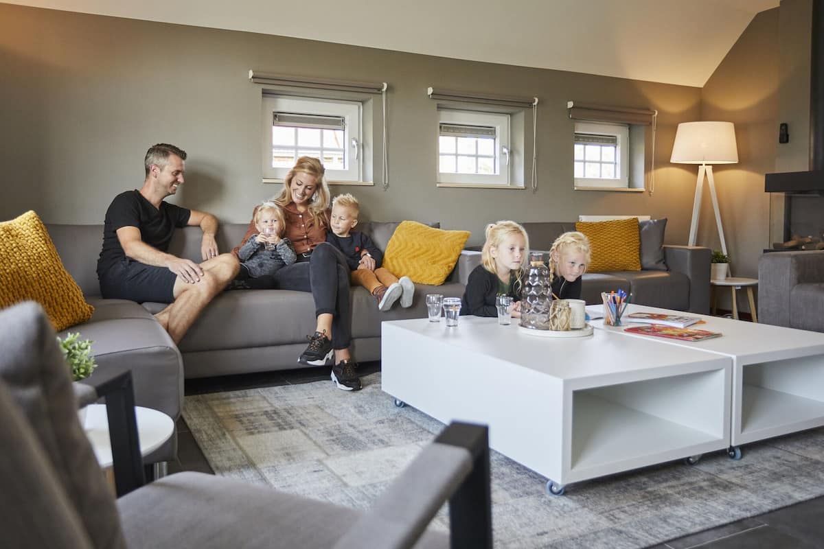A family sitting on a grey sofa in a modern living room with a white coffee table, grey walls, and a lamp.
