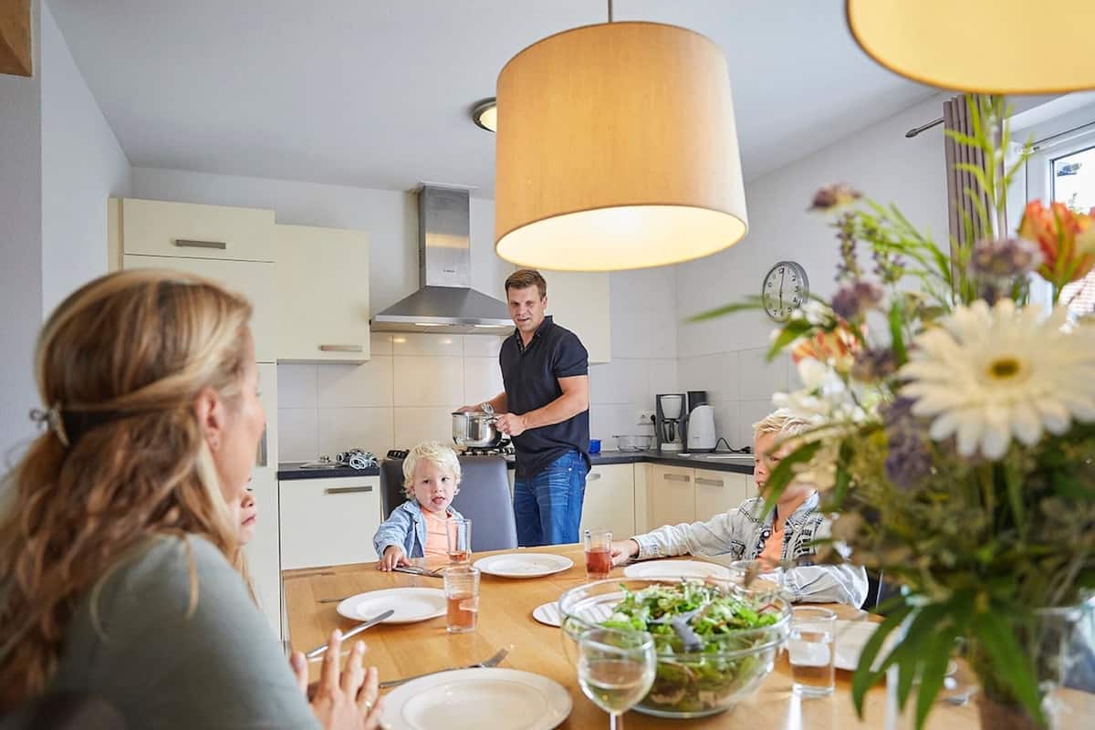 A family dining in a modern kitchen with a central island, a hanging light fixture, and a clock on the wall.