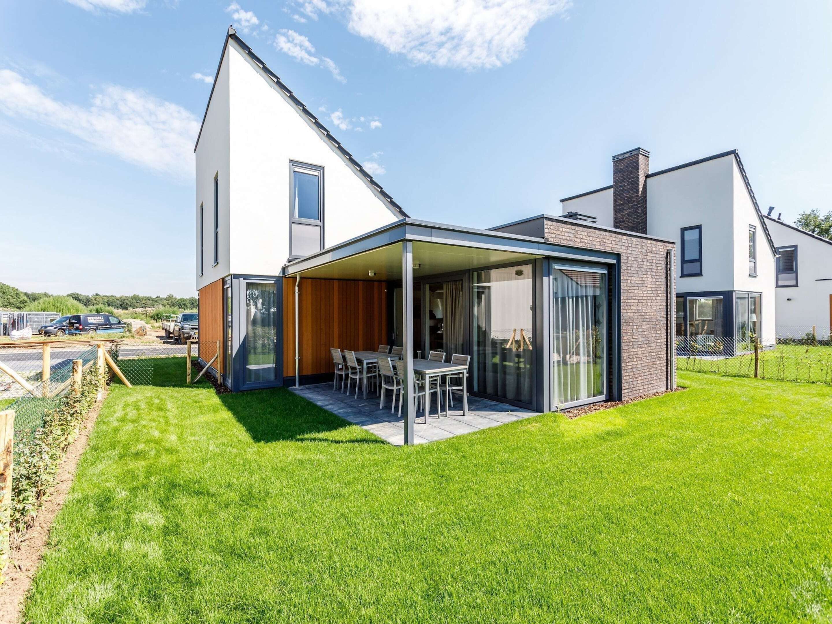 Ein modernes Haus mit überdachter Terrasse, einem Rasen und blauem Himmel.