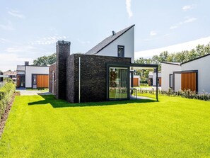 Ein modernes Haus mit einer großen Glasdoor, einem Backsteinsschornstein und einem gepflegten Rasen.