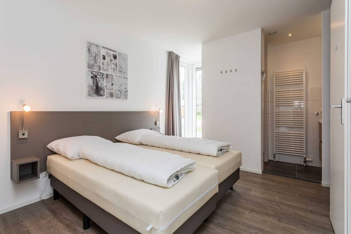 A double bed with a headboard, bedside tables with lamps, a wall-mounted artwork, and a bathroom with a towel rack.