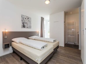 A double bed with a headboard, bedside tables with lamps, a wall-mounted artwork, and a bathroom with a towel rack. - Nice Villa With Sauna, Whirlpool & Steam Shower (Roggel)