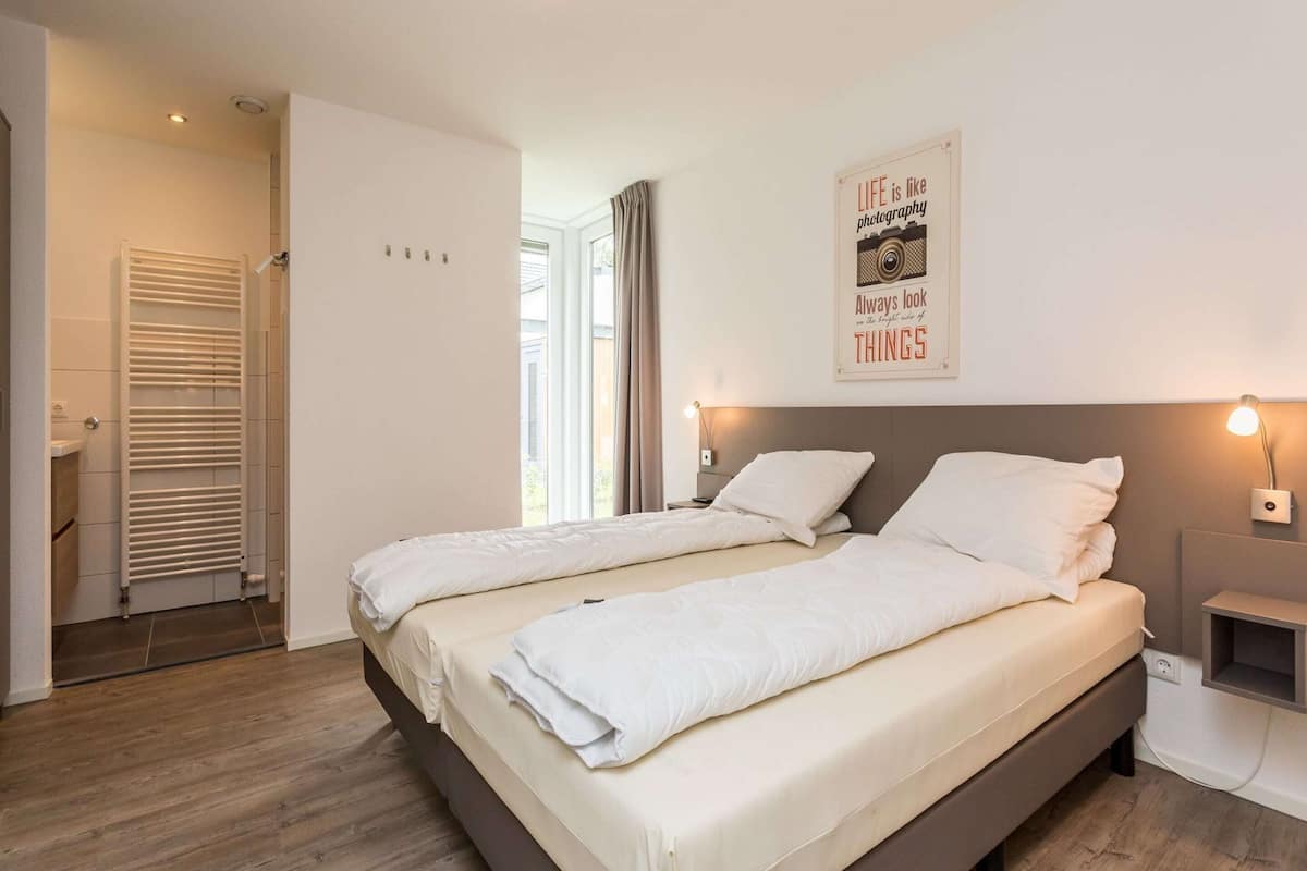 A modern bedroom with two beds, a large window, a radiator, and a motivational poster on the wall.