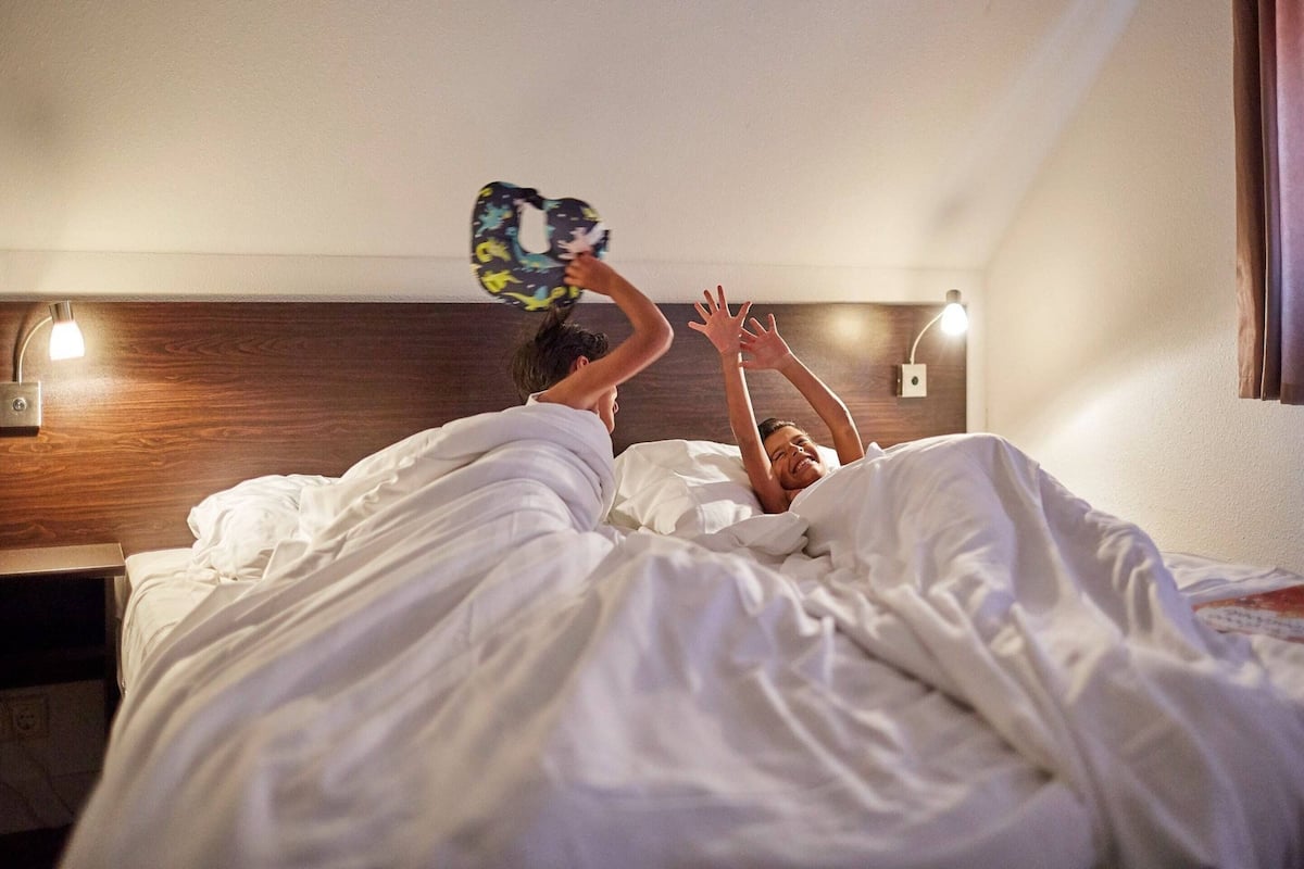 A hotel room with a wooden headboard, a bedside lamp, and a bed with white bedding.
