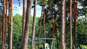 Un parque infantil con columpios, tobogán y estructura para escalar, rodeado de árboles altos.