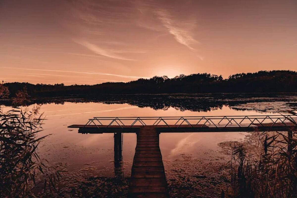 Un muelle de madera se adentra en una masa de agua tranquila, con un atardecer en el fondo.