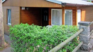 Una cabaña de madera con techo inclinado, una puerta principal y un pequeño porche.