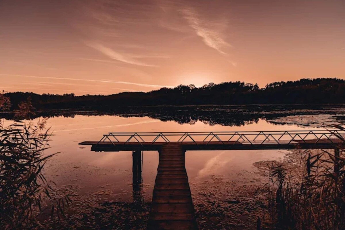 A wooden pier extending over calm water with a sunset in the background.