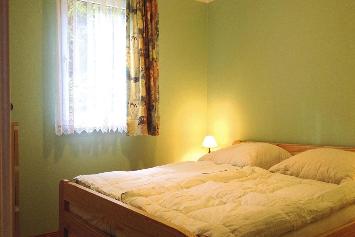 A single bed with a wooden frame and a white duvet in a room with green walls.