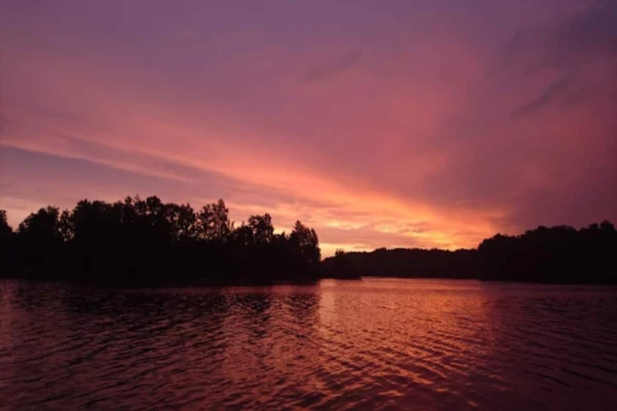 A sunset over a body of water with a silhouette of trees on the horizon.