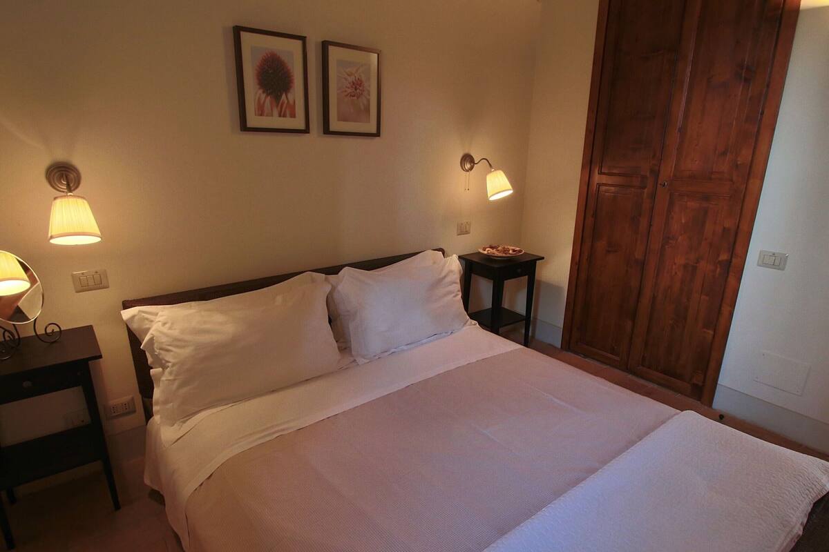 A neatly made bed with white linens, two wall-mounted lamps, and a wooden wardrobe.