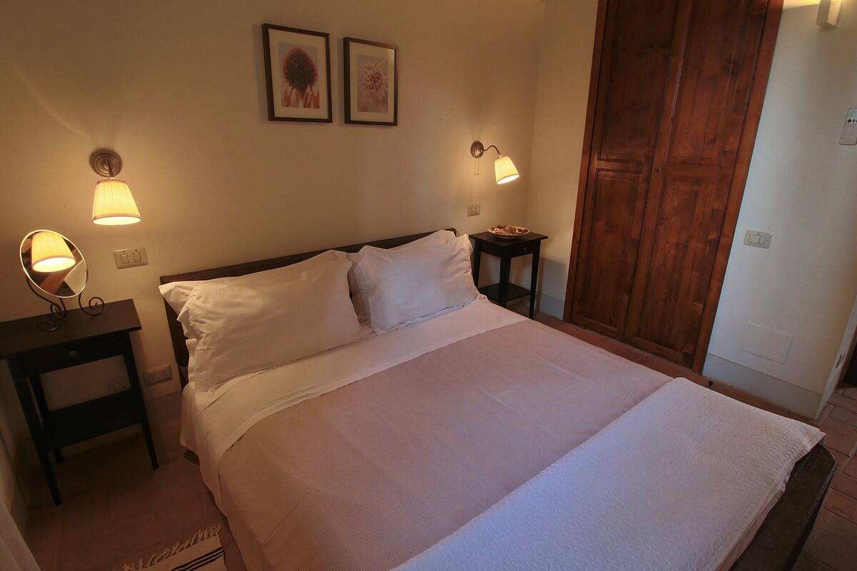 A neatly made bed with white linens, two bedside lamps, and a wooden wardrobe in a hotel room.