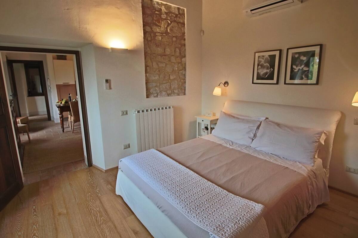 A bedroom with a large bed, a stone accent wall, two wall-mounted lamps, and a radiator.