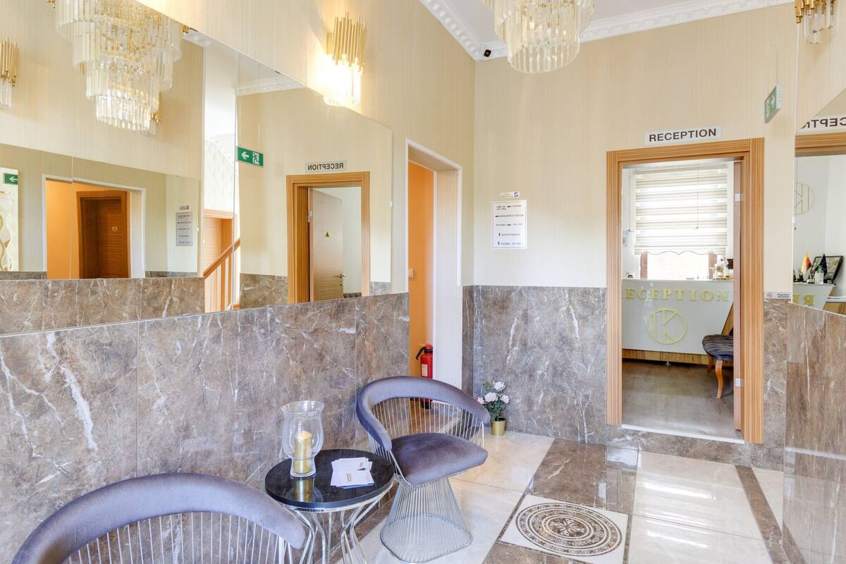 A reception area with marble flooring, two grey chairs, a small table with a candle, and a chandelier.