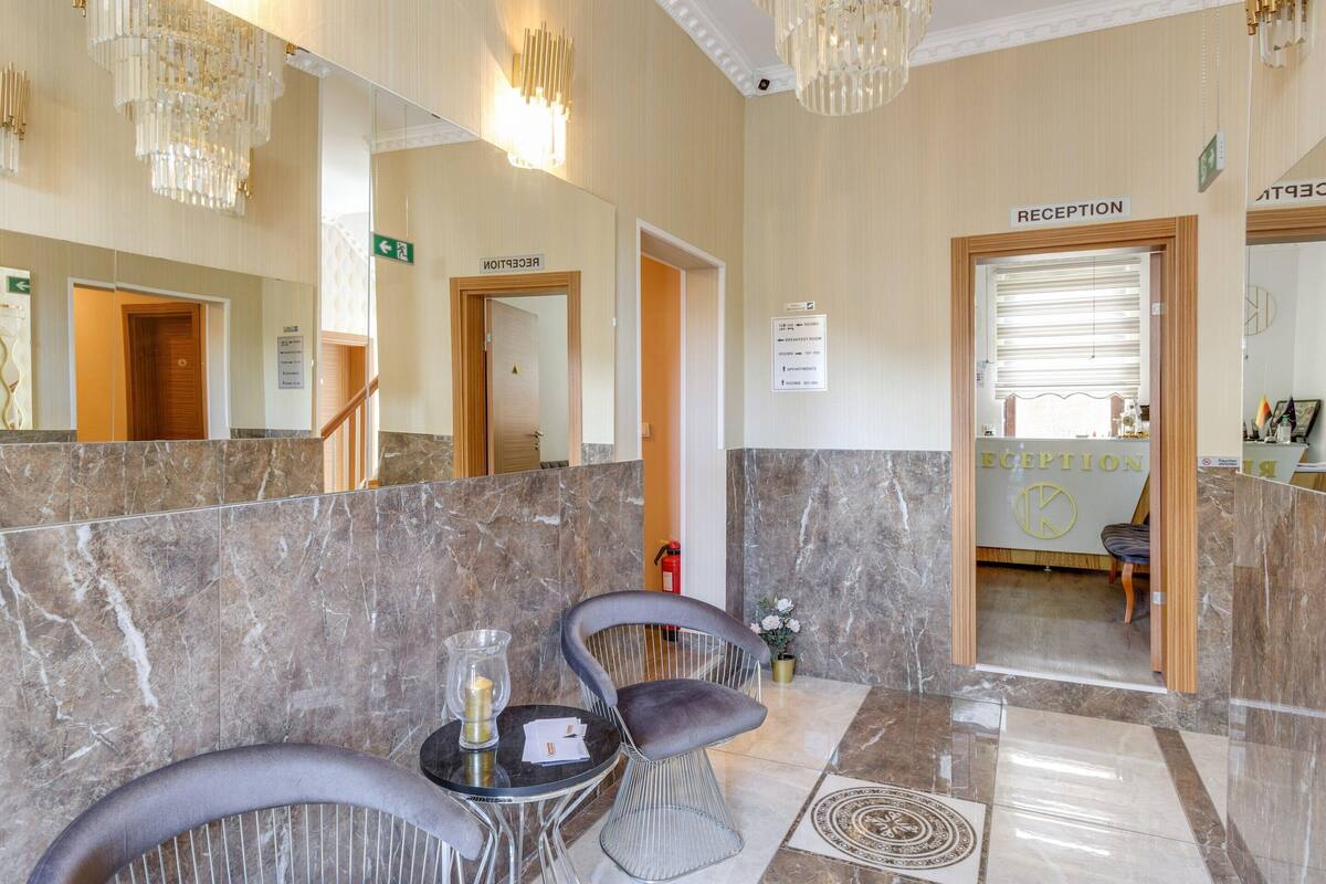 A reception area with marble flooring, two grey upholstered chairs, a small table with a candle, and a reception desk.