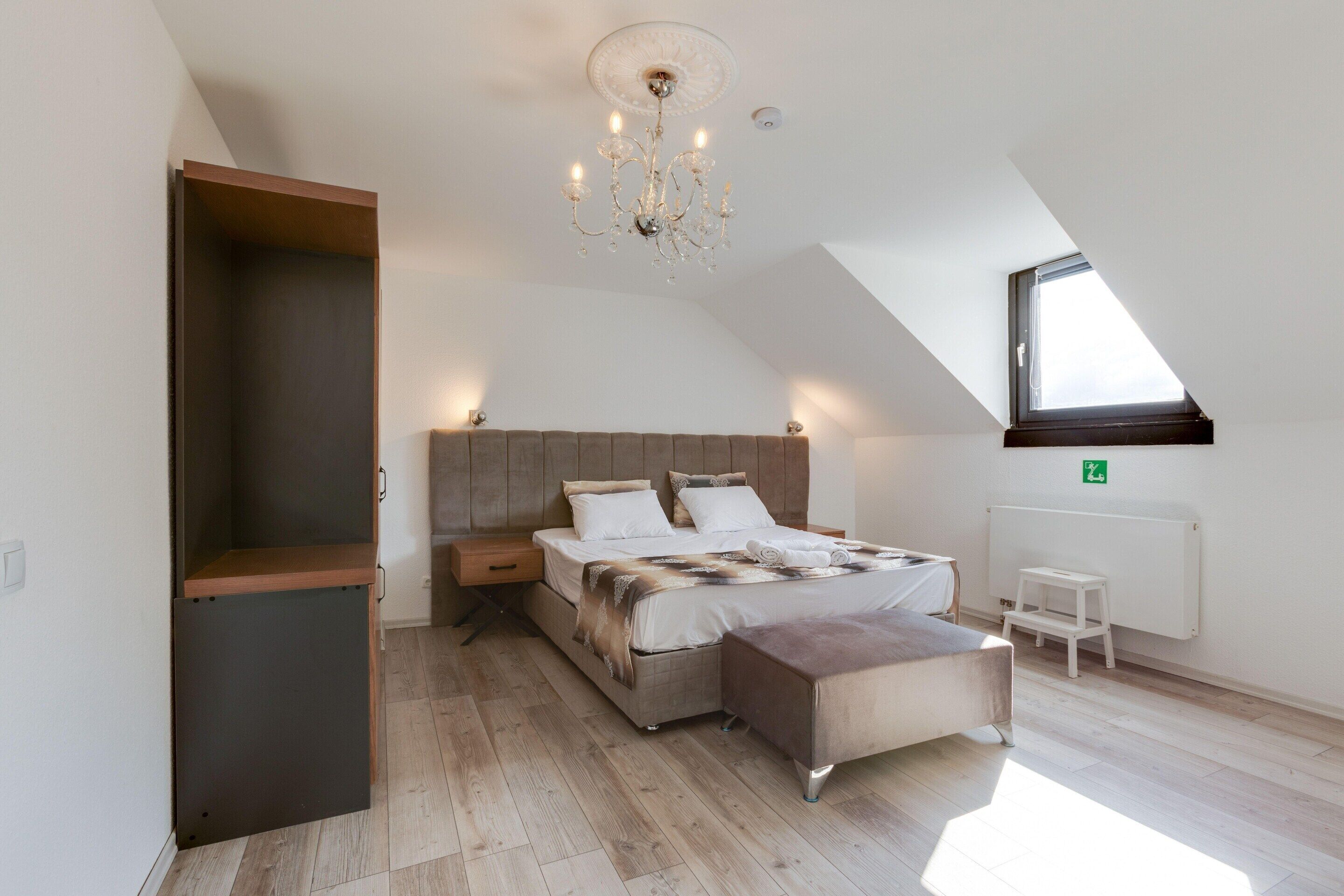 Un dormitorio con techo inclinado, una cama con cabecera de madera, un banco, una mesita y un radiador.