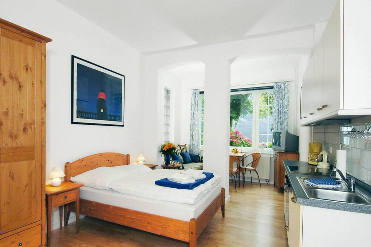 A bedroom with a wooden bed, a nightstand, a desk, and a window with curtains.