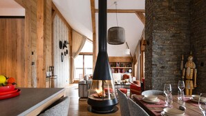 Un ambiente accogliente con un tavolo da pranzo in legno apparecchiato per due, un piano cottura nero con un fuoco visibile e una parete in mattoni rustici.