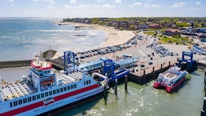 Un molo traghetti con una grande nave, un pontile e una spiaggia con auto e persone.