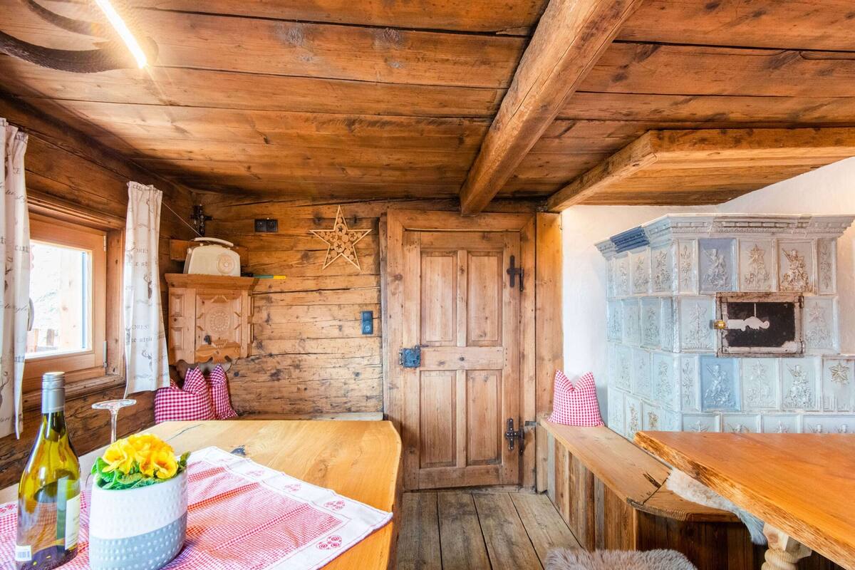A rustic wooden interior with a wooden door, a bench, and a table with a bottle and flowers.