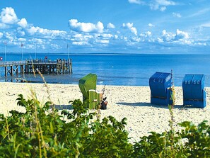 Een strand met een pier, groene en blauwe strandstoelen, en een helderblauwe lucht.