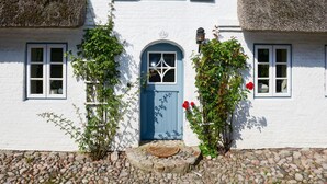 A white building with blue shutters, a blue door, and a stone foundation. - Semi-detached Houses, Oldsum auf Fohr (Oldsum)