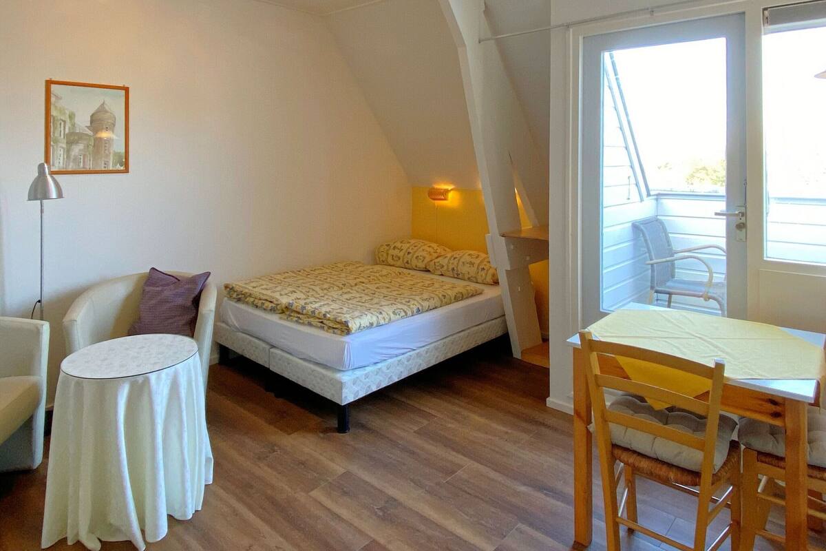 Una habitación pequeña y funcional con cama, una silla, una mesita y una ventana.