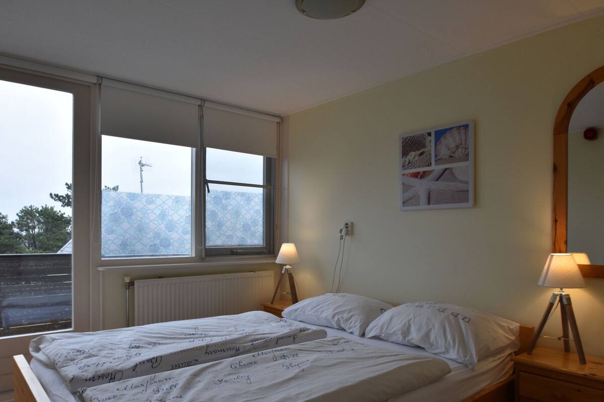 Un dormitorio con una cama, dos lámparas de noche, un ventanal y un cuadro en la pared.