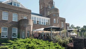 Een historisch gebouw met een opvallende toren, grote ramen en buiten zitplaatsen.