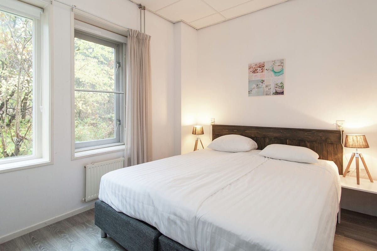 Un dormitorio con una cama grande, dos lámparas de noche, una ventana con cortinas y un cuadro colgado en la pared.