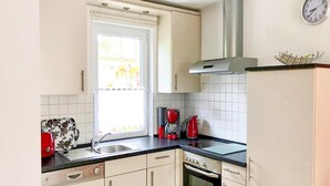 Une cuisine avec des meubles blancs, une hotte de cuisinière en acier inoxydable, une machine à café rouge et une fenêtre donnant sur un paysage verdoyant.