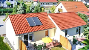 Une maison à deux étages avec un toit recouvert de tuiles rouges, un balcon avec des chaises vertes et un parasol jaune.