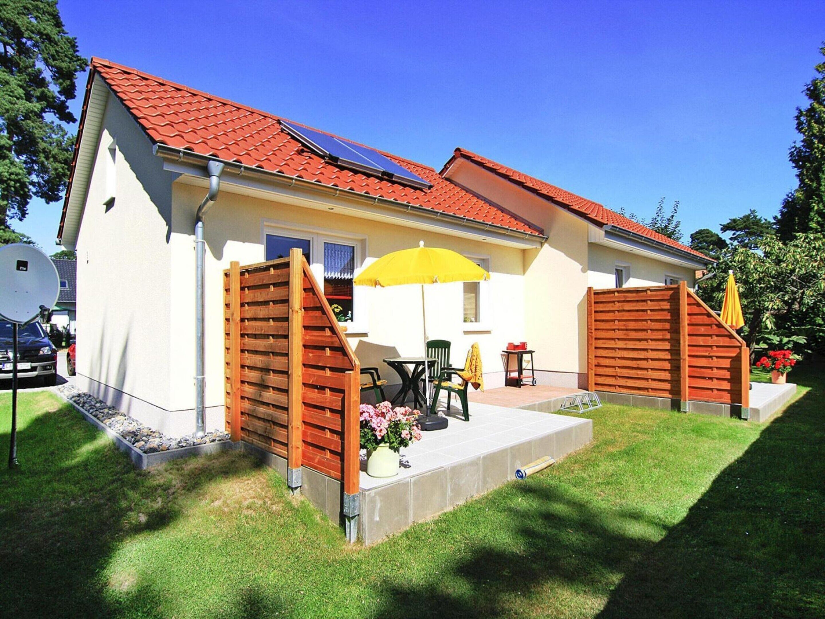 A two-story house with a red-tiled roof, a covered patio with a yellow umbrella, and a small garden area with flowers.