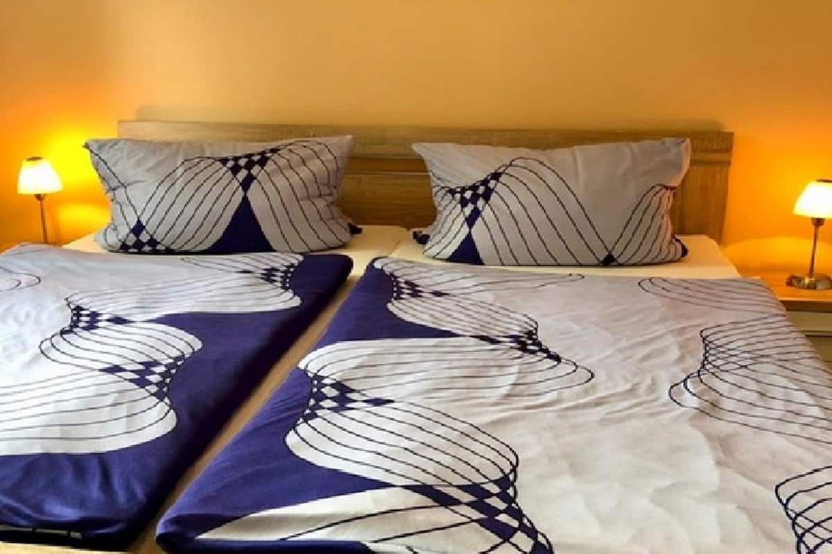 A bed with striped pillows and a patterned bedspread, a framed picture above the bed, and two bedside lamps.