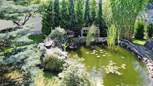 Un jardin paisible avec un étang, différents arbustes et un petit pont.