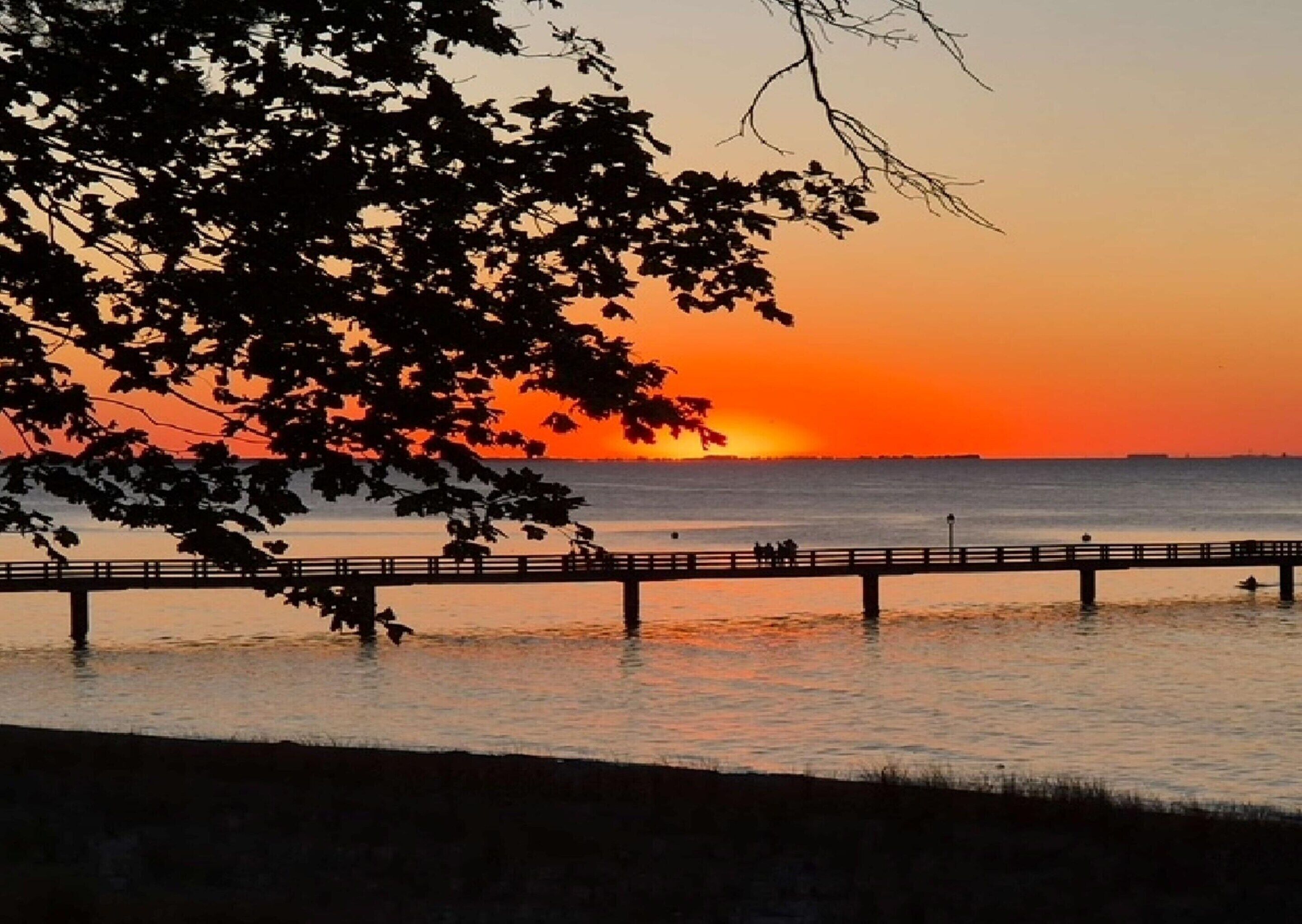 A sunset over water with a pier extending into the scene.