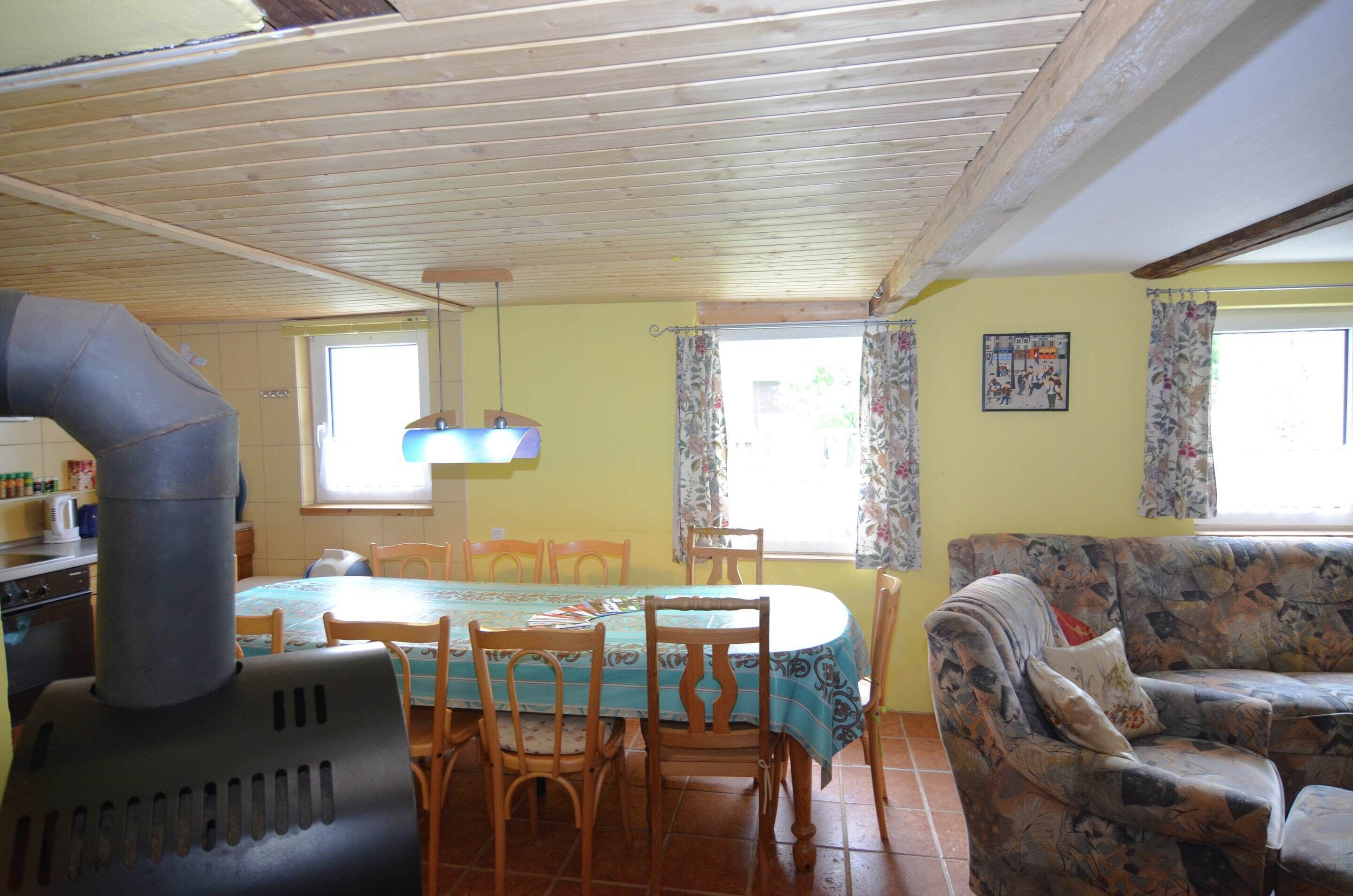 A dining area with a wooden table and chairs, a sofa, and a kitchen area with a stove.