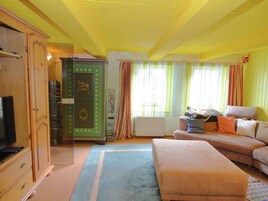 Una habitación con televisión, un aparador verde, sofá y una ventana con cortinas.