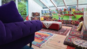 A cozy reading nook with a purple armchair, a red sofa, and a variety of colorful rugs.