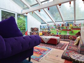 Un rincón acogedor para leer con un sillón púrpura, un sofá rojo y varios alfombras coloridas.