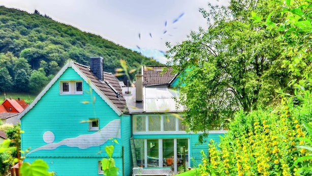 A turquoise house with a sloped roof, a chimney, and a large glass window.