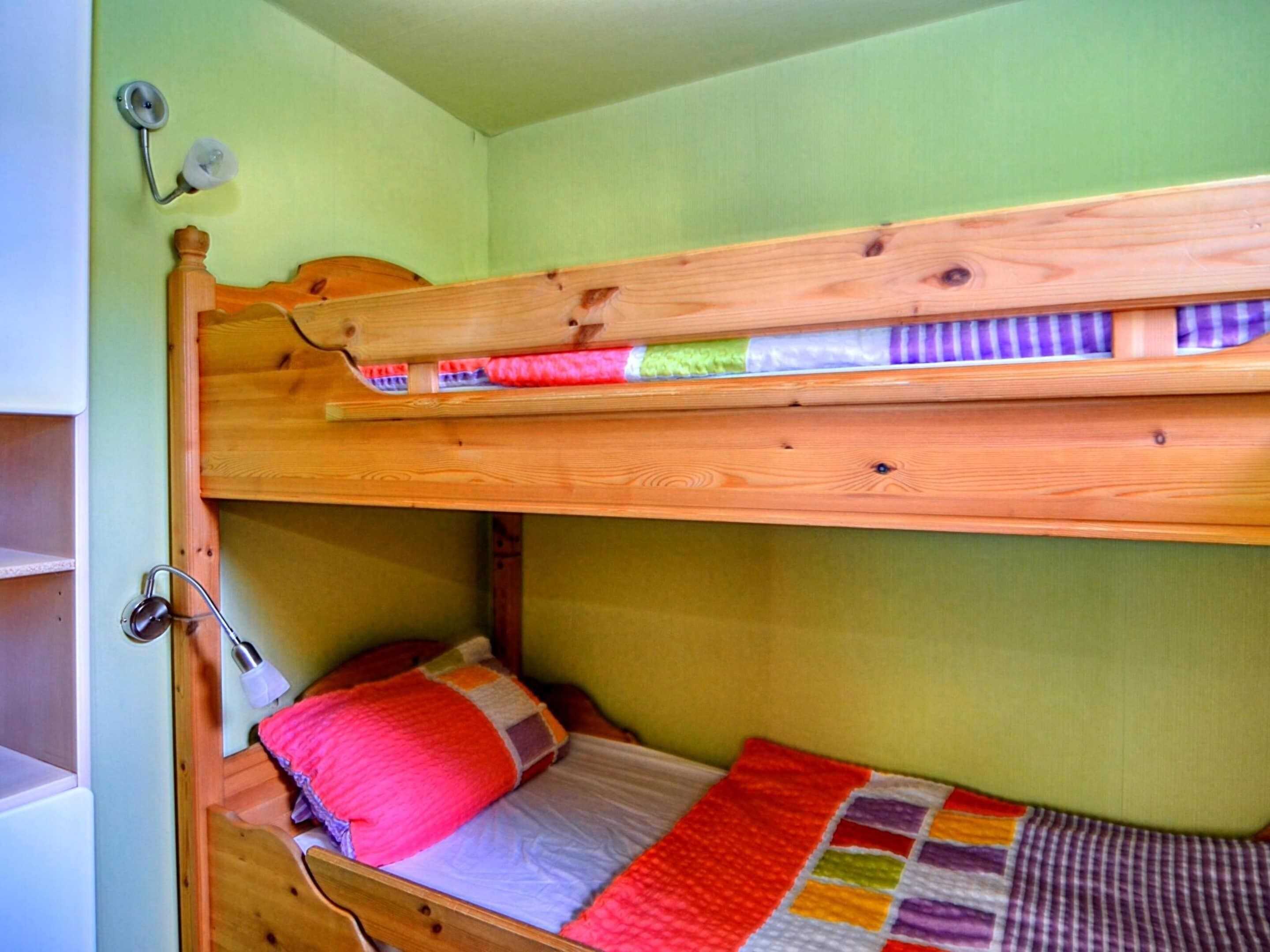 A bunk bed with a wooden headboard, a lower bunk with a red pillow, and a quilt with a checkered pattern.