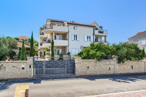 Un edificio residencial de varios pisos con un muro de piedra, una entrada con reja y balcones.