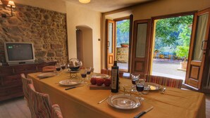 A dining area with a table set for two, a stone wall, and a television in the corner. - Modern Holiday Home in Castelfranco di Sopra With Swimming Pool (Castelfranco Piandisco)