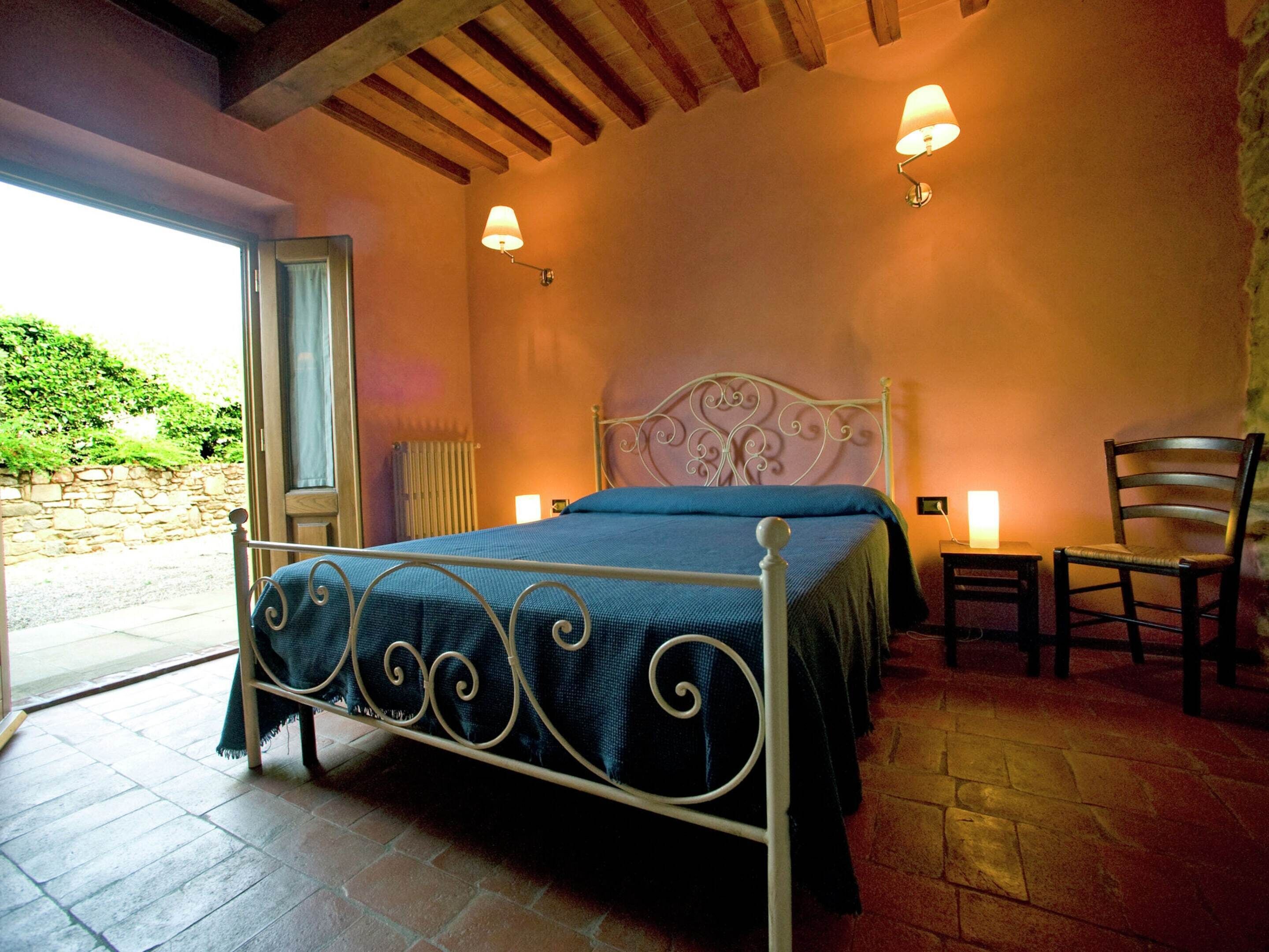 A bedroom with a bed, two wall-mounted lamps, a chair, and a window.