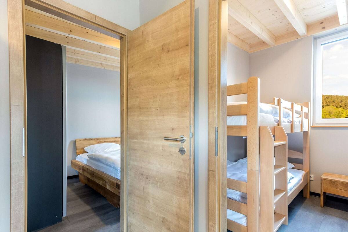 A compact bedroom with a wooden bunk bed, a single bed, and a door leading to another room.